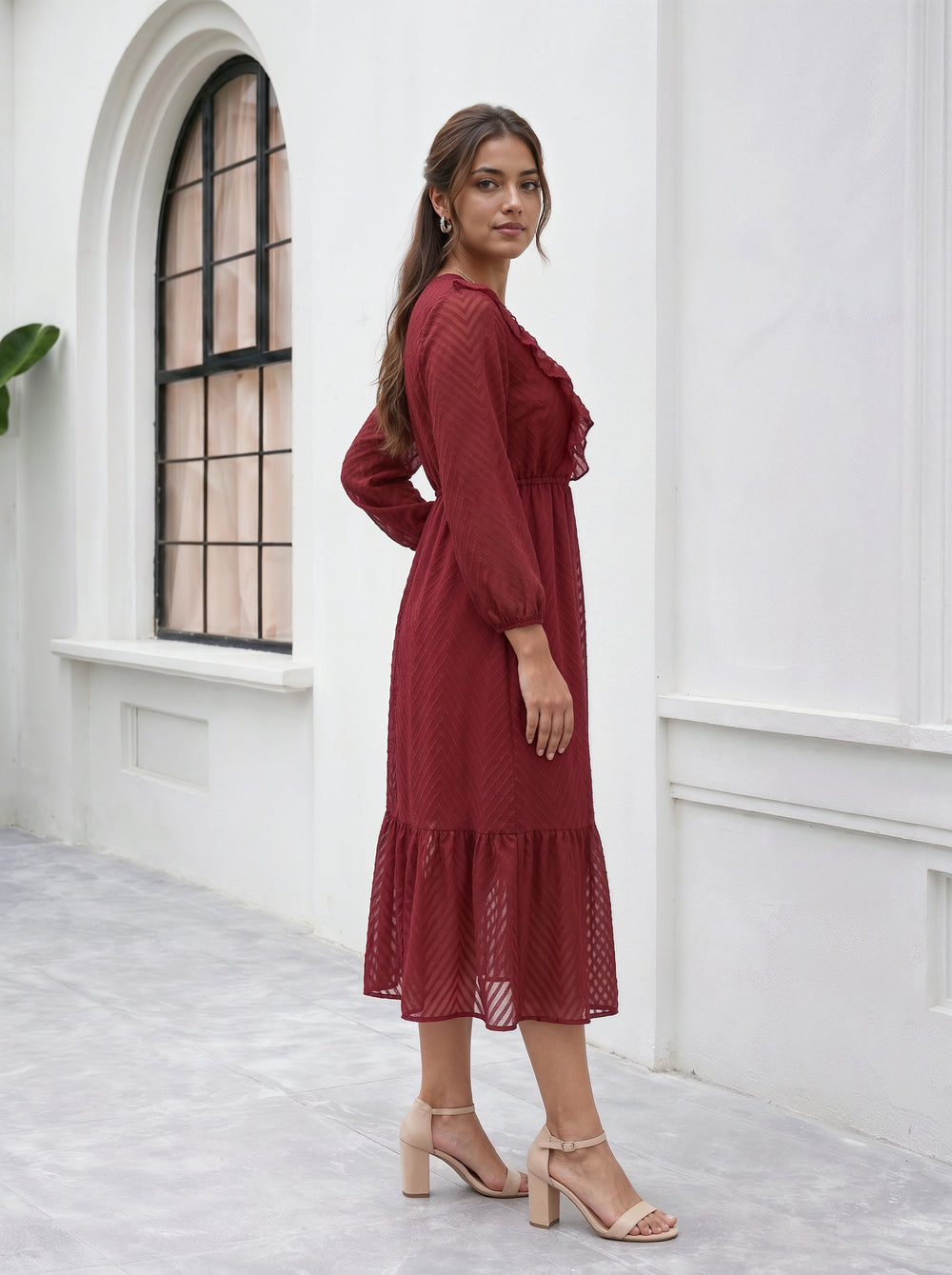 Woman in a red dress standing in a white room with a window.