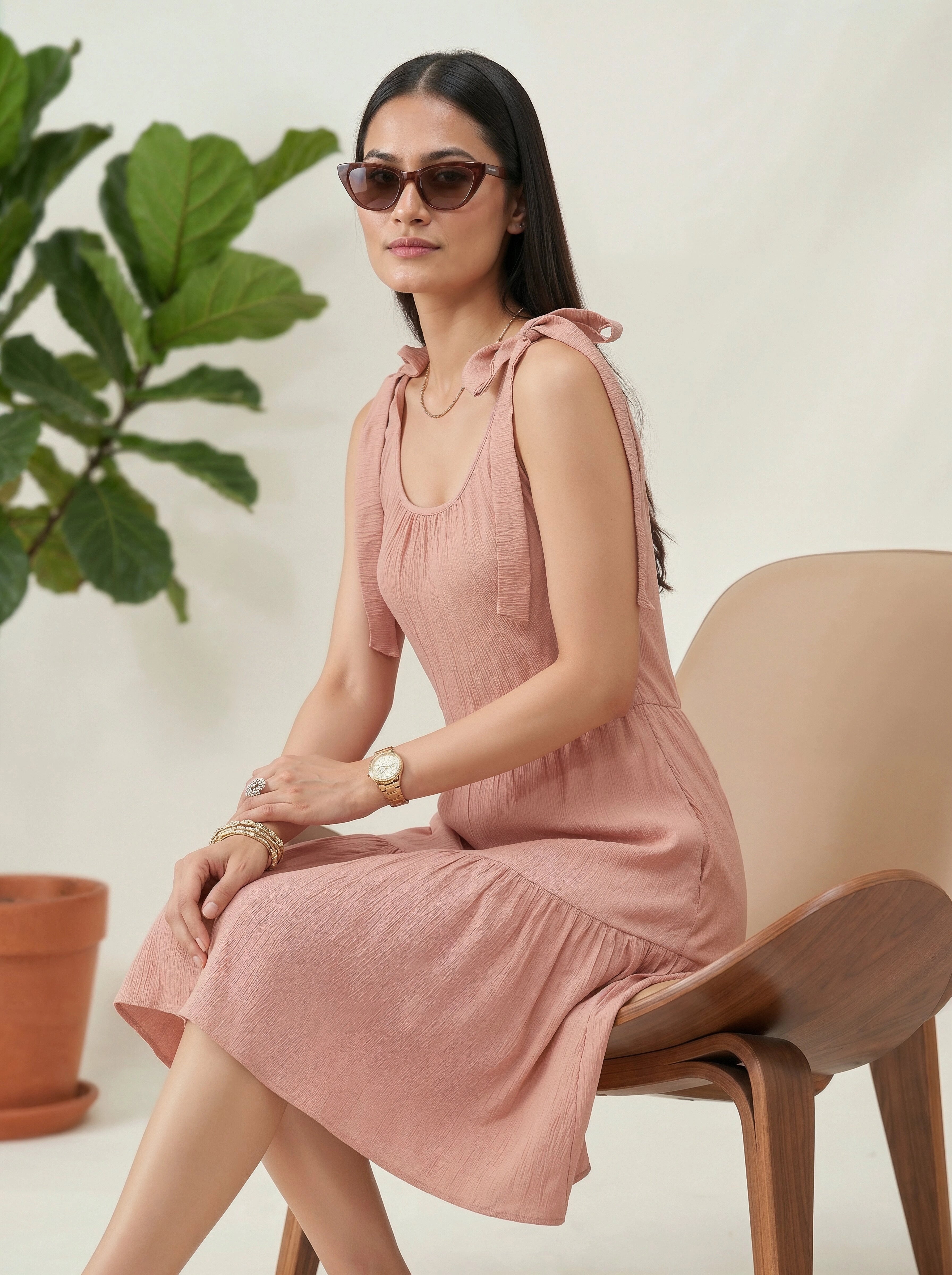 Woman in a pink dress sitting on a chair with a plant in the background