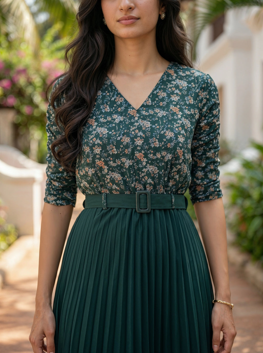 Woman wearing a green floral blouse and pleated skirt outdoors.