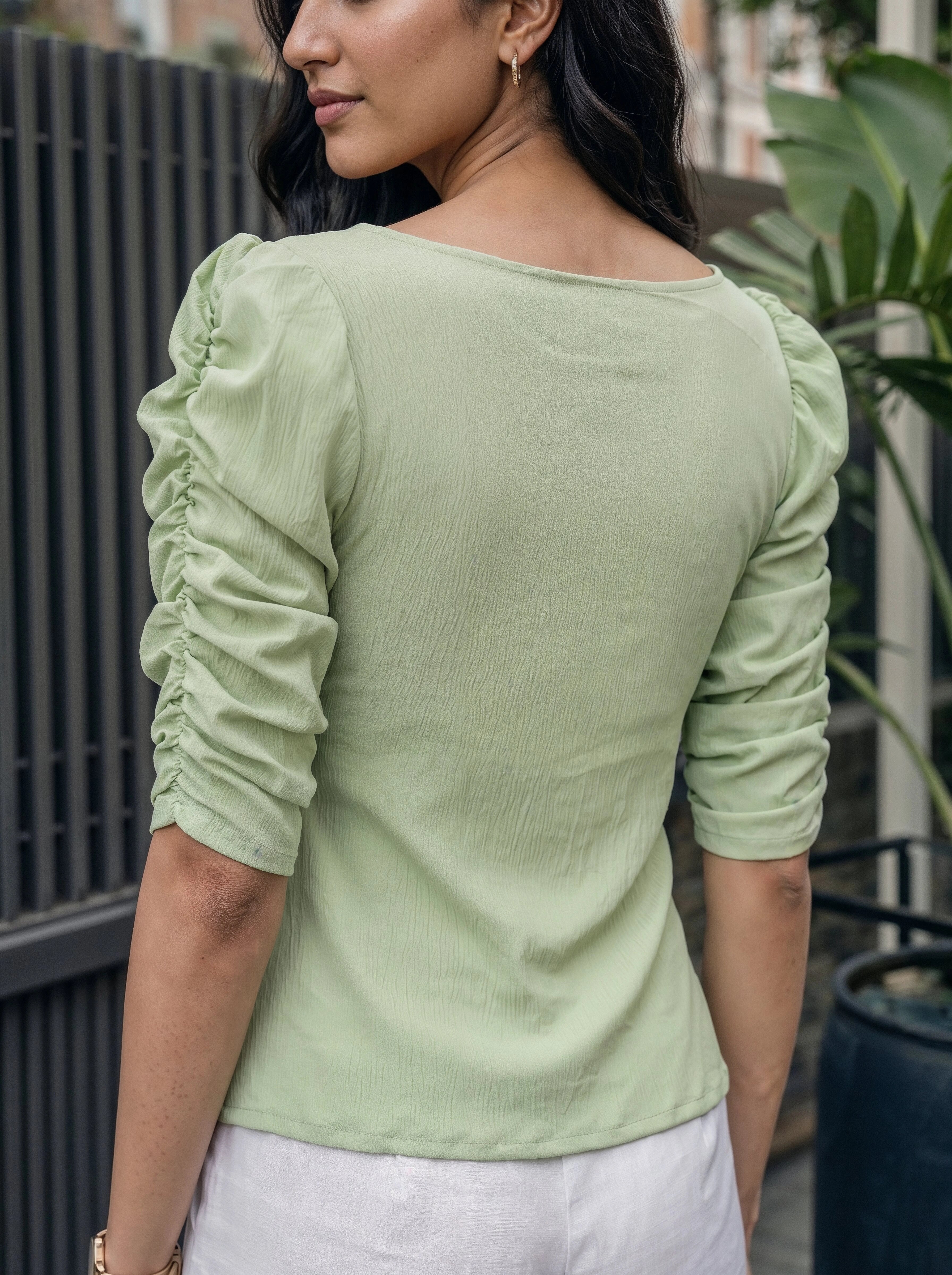 Woman wearing a light green long-sleeve top with ruched sleeves, standing outdoors.