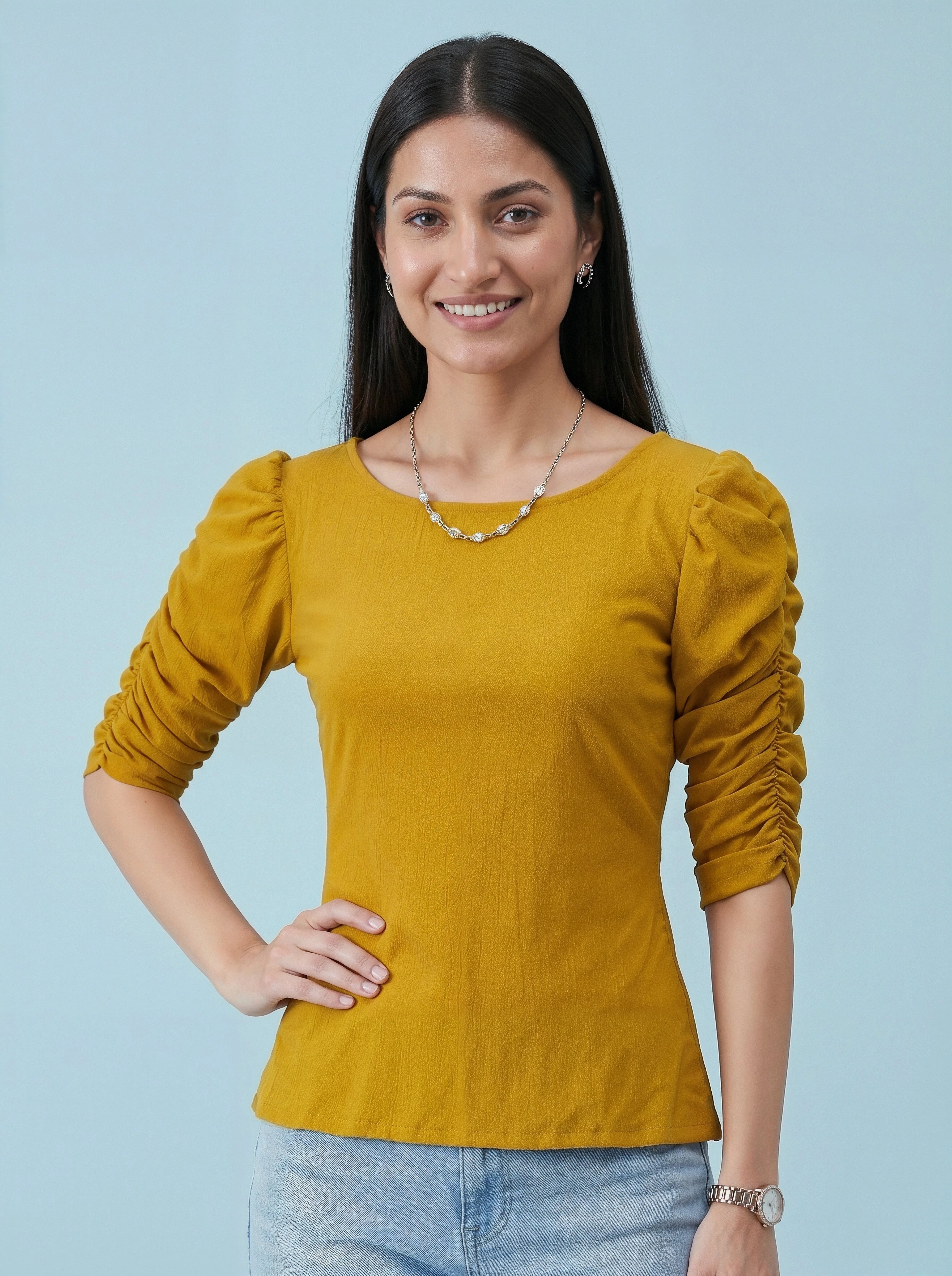 Woman wearing a mustard yellow top with ruched sleeves against a light blue background
