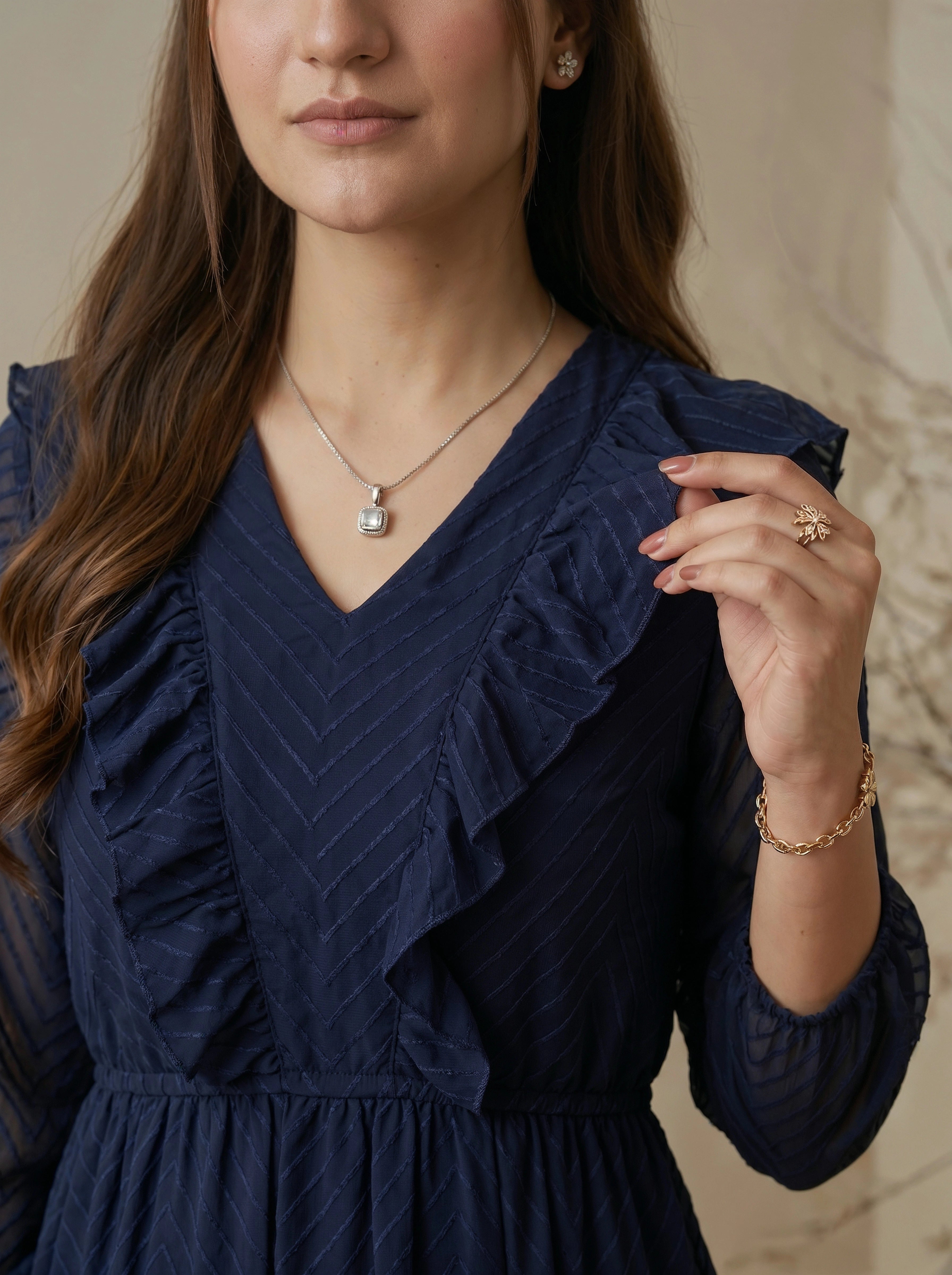 Woman wearing a navy blue dress with ruffled details, accessorized with jewelry.