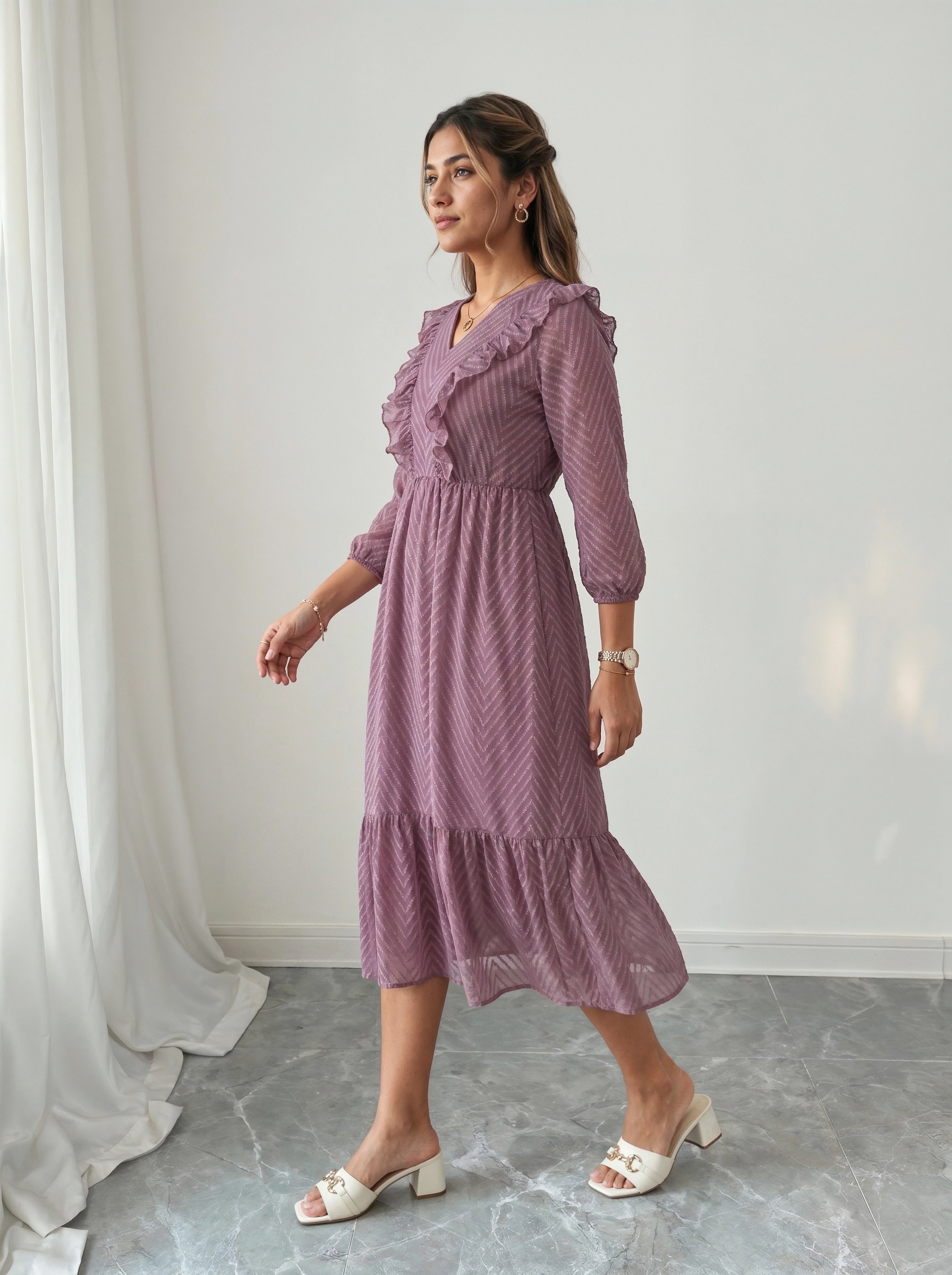Woman wearing a purple dress standing in a room with white curtains and gray floor.
