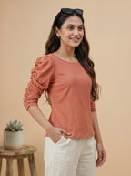 Woman wearing a rust-colored blouse with puffed sleeves against a beige background