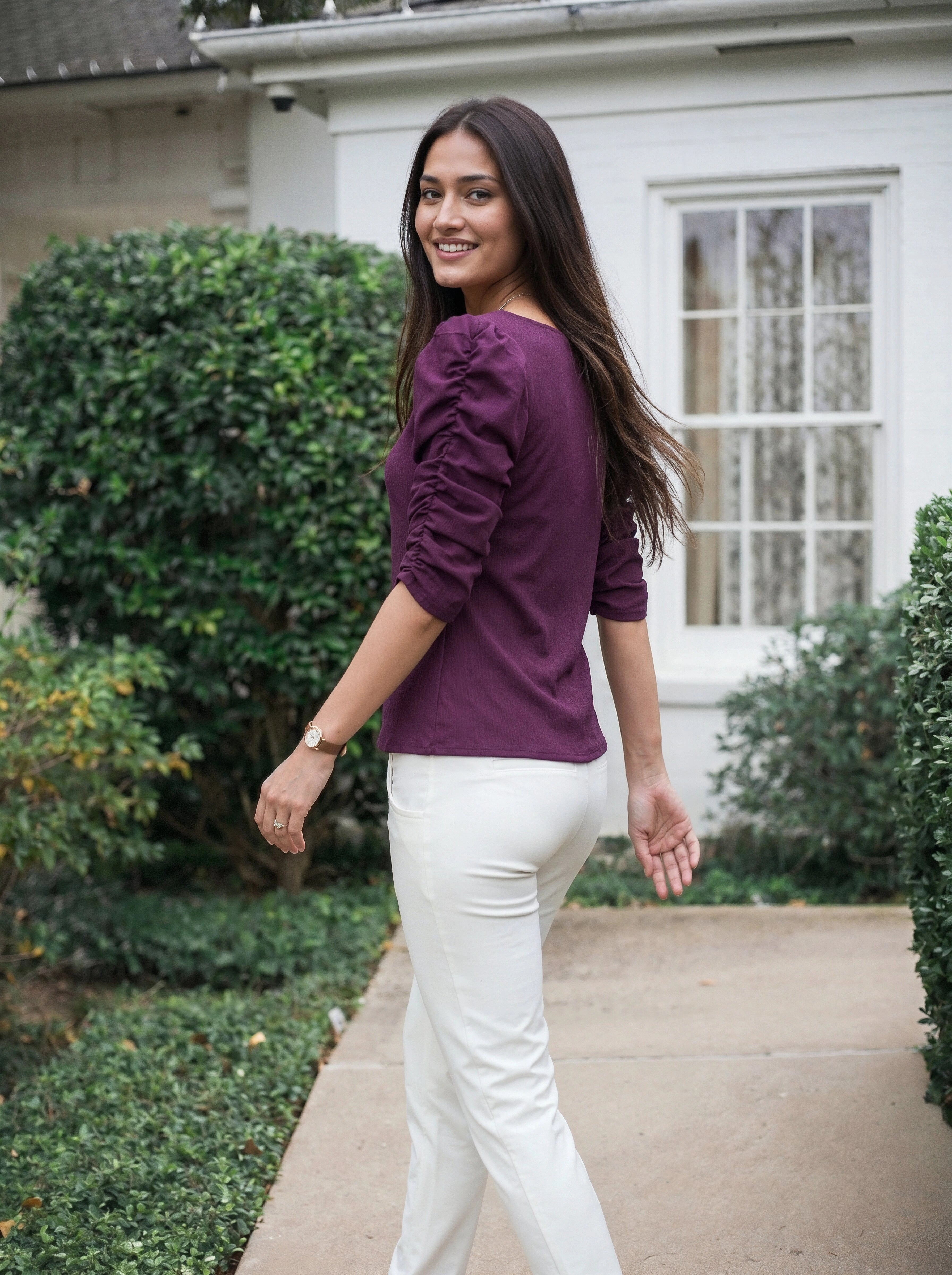 Woman wearing a purple top and white pants walking outdoors.
