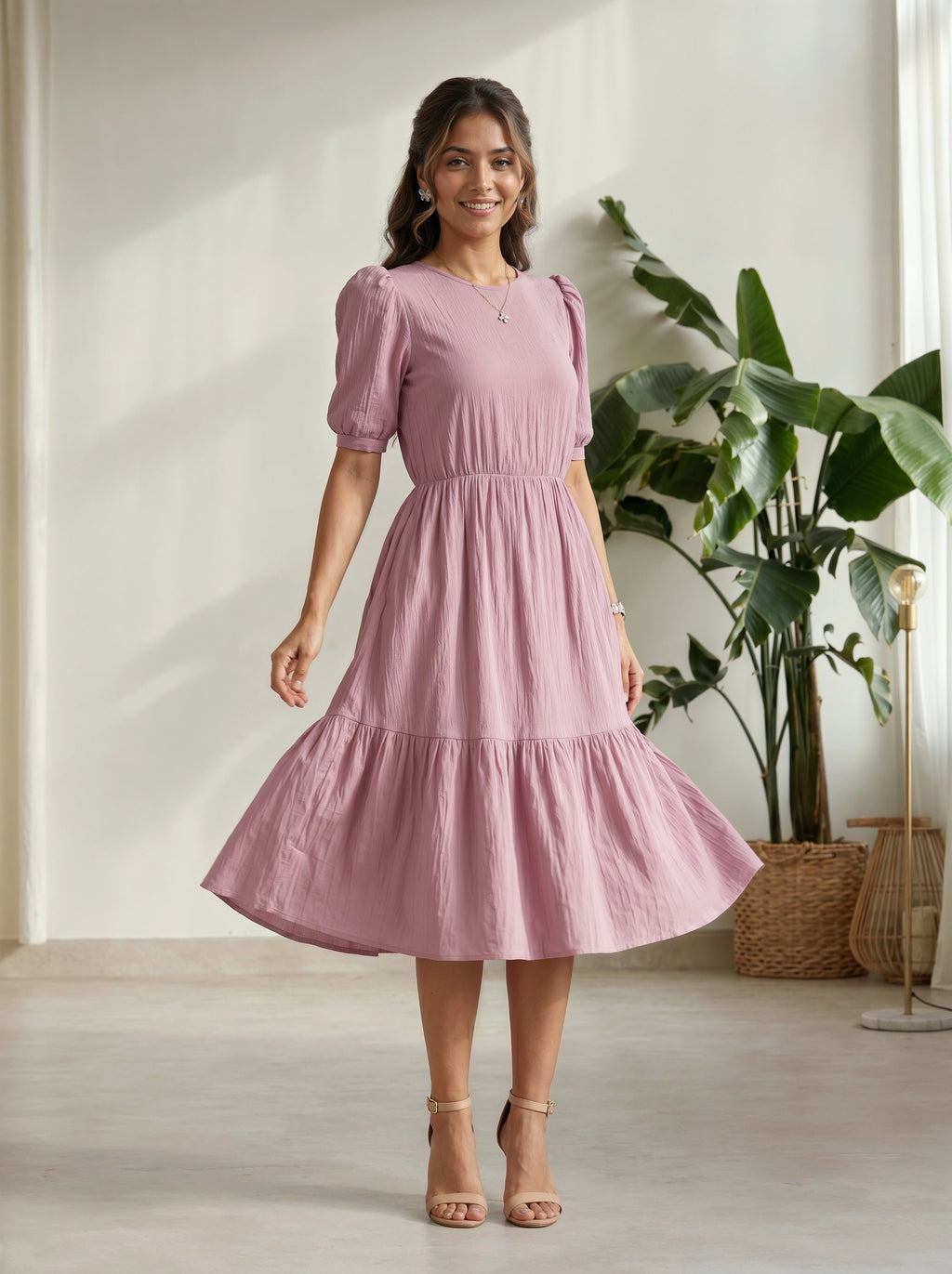 Woman wearing a pink dress standing in a room with a plant and light-colored floor.