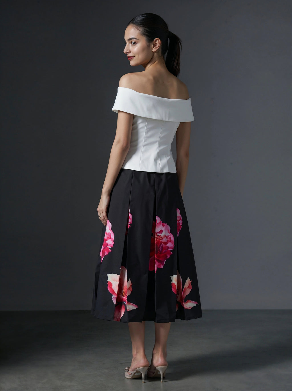 Woman wearing a white off-shoulder top and black floral skirt against a gray background