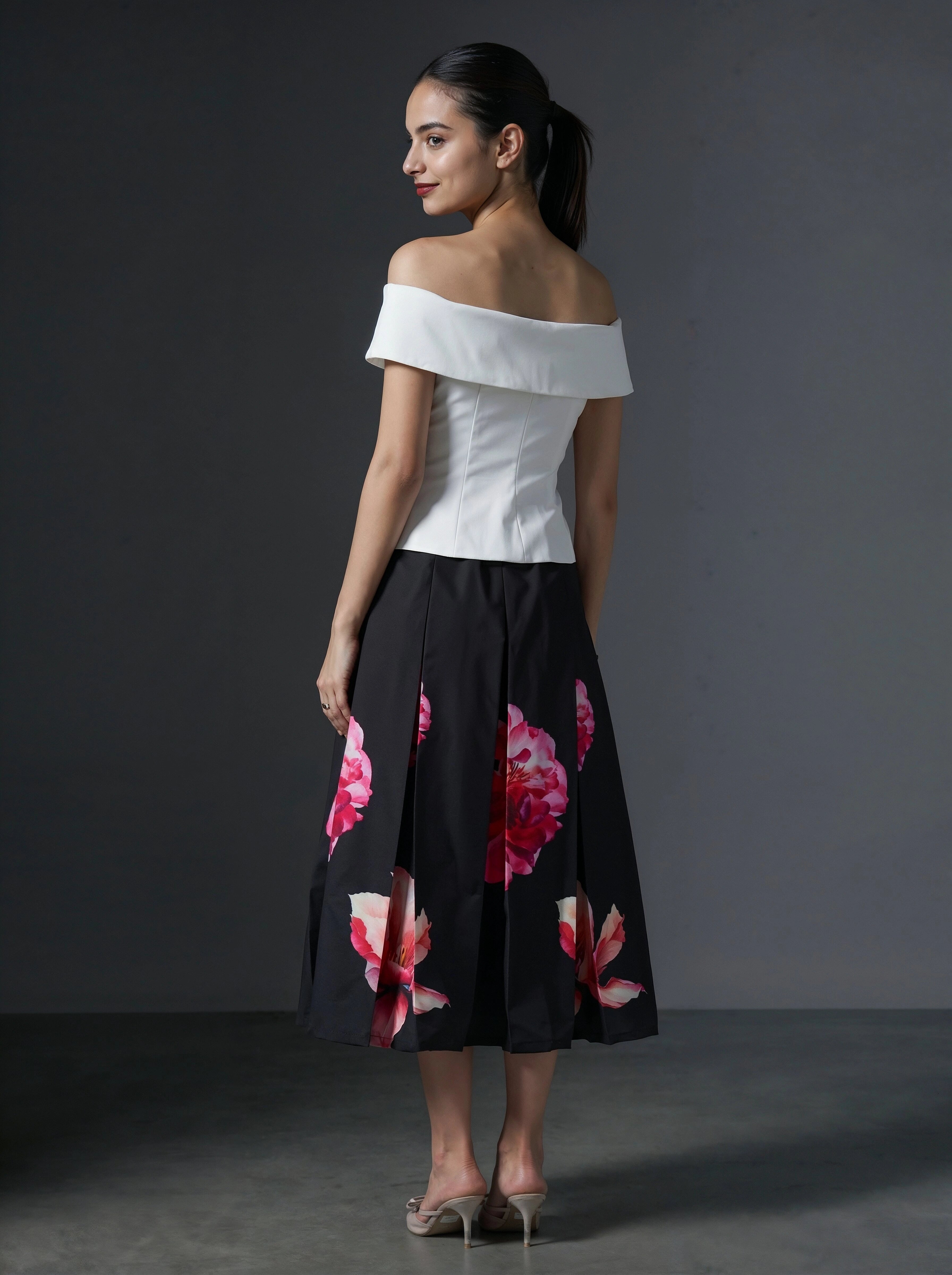 Woman wearing a white off-shoulder top and black floral skirt against a gray background