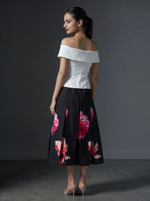 Woman wearing a white off-shoulder top and black floral skirt against a gray background