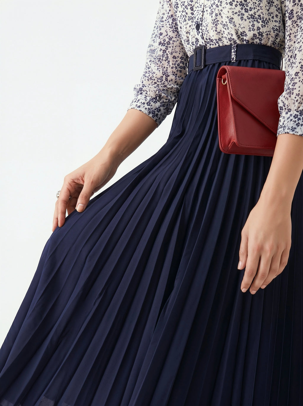 Person wearing a navy pleated skirt and holding a red handbag against a light background