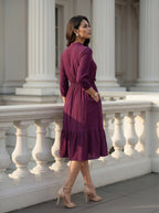Woman in a purple dress standing on a classical building's steps.