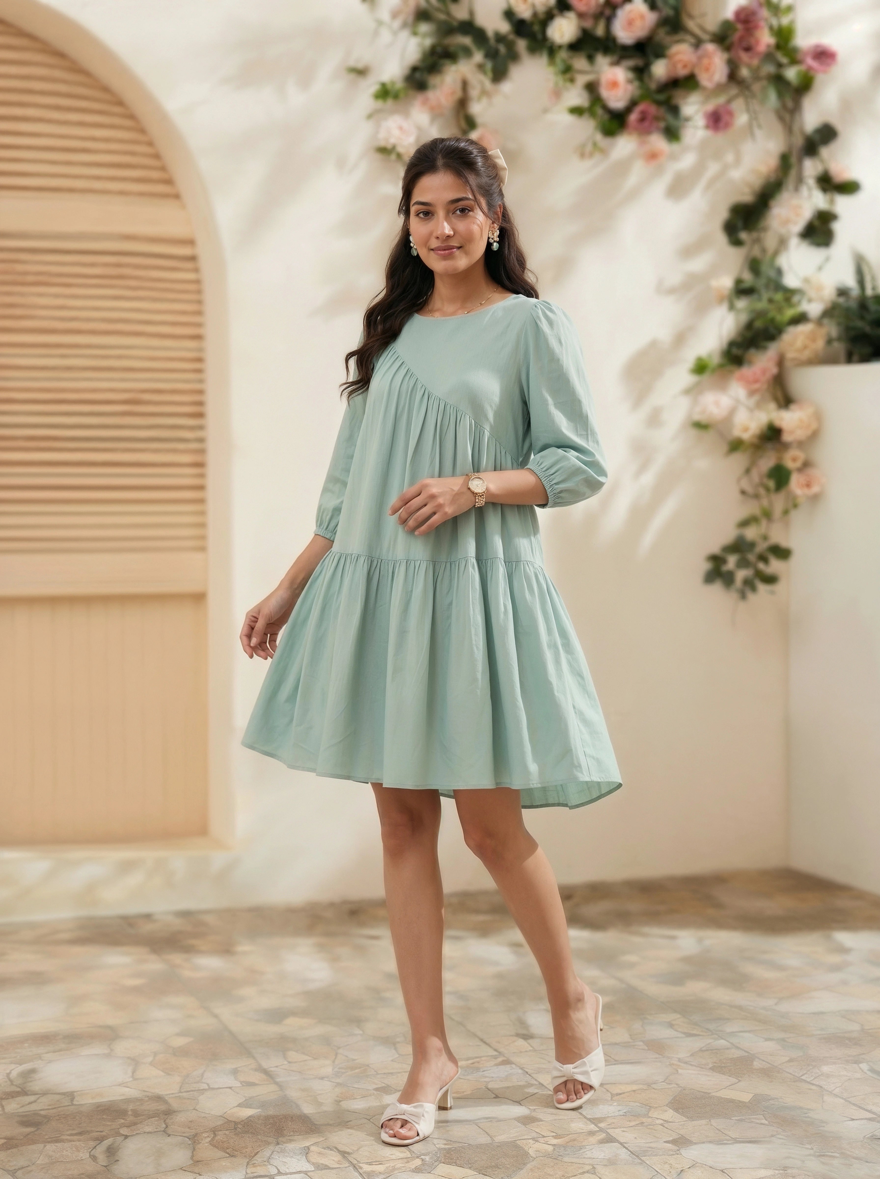Woman in a light green dress standing in a decorated indoor setting with flowers.