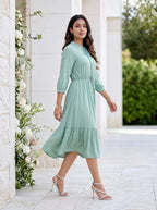 Woman in a light green dress walking outdoors near a decorative floral arrangement.