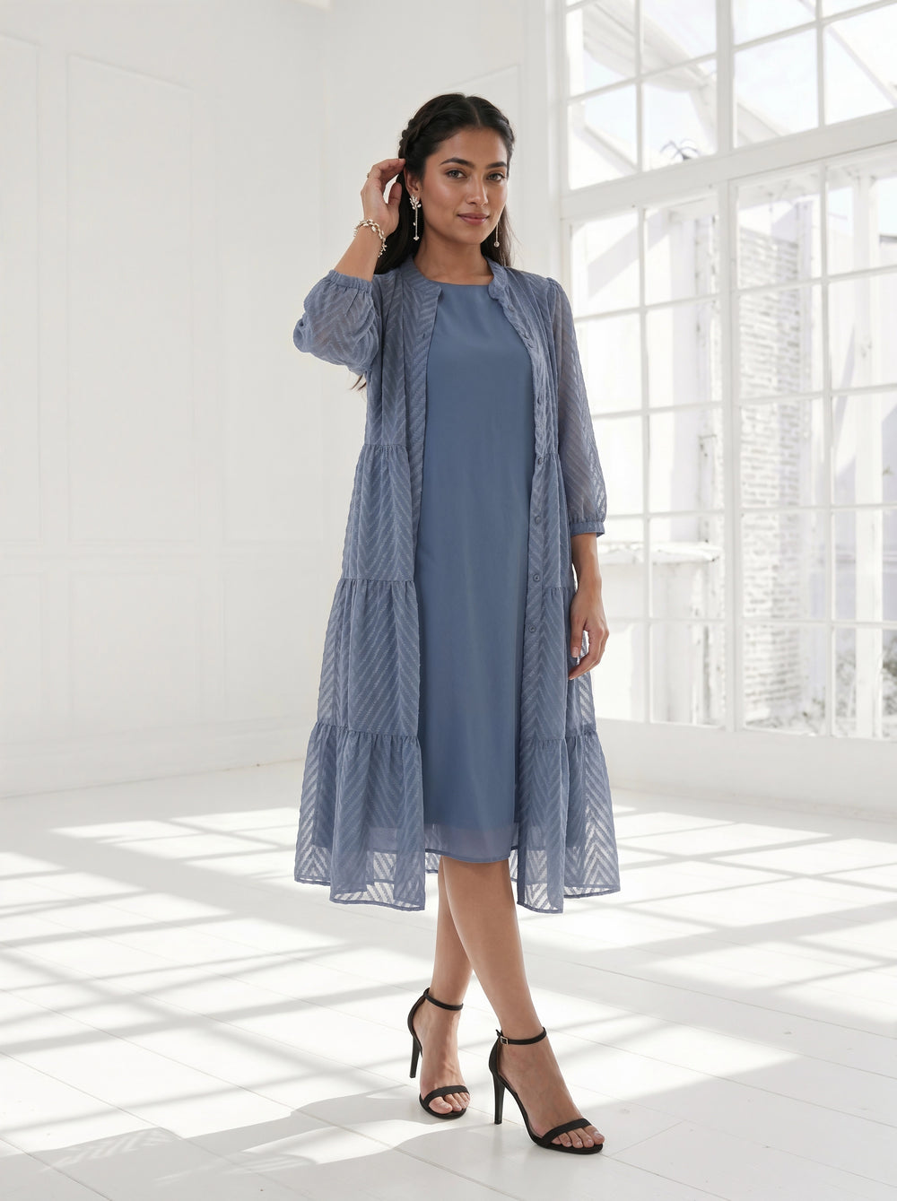 Woman wearing a blue dress with a matching cardigan in a bright room.