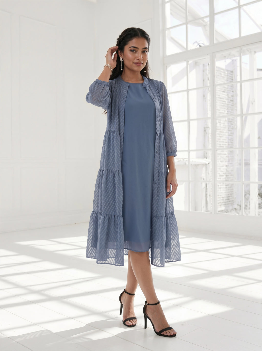 Woman wearing a blue dress with a matching cardigan in a bright room.