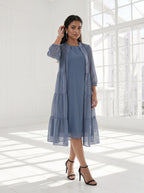 Woman wearing a blue dress with a matching cardigan in a bright room.