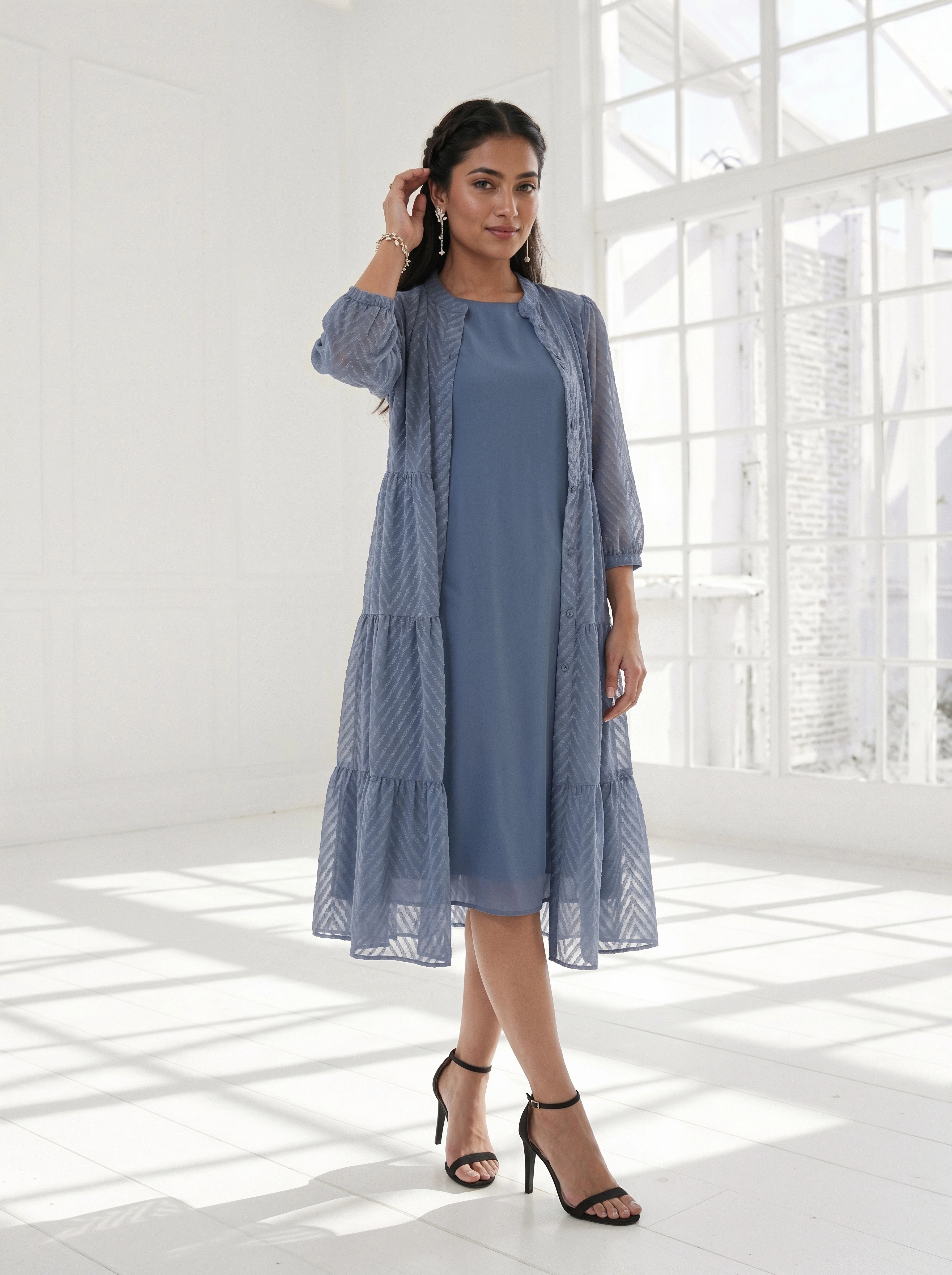 Woman wearing a blue dress with a matching cardigan in a bright room.