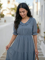 Woman wearing a blue dress with a white building and plants in the background