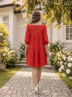Woman in a red dress walking on a stone path in a garden.