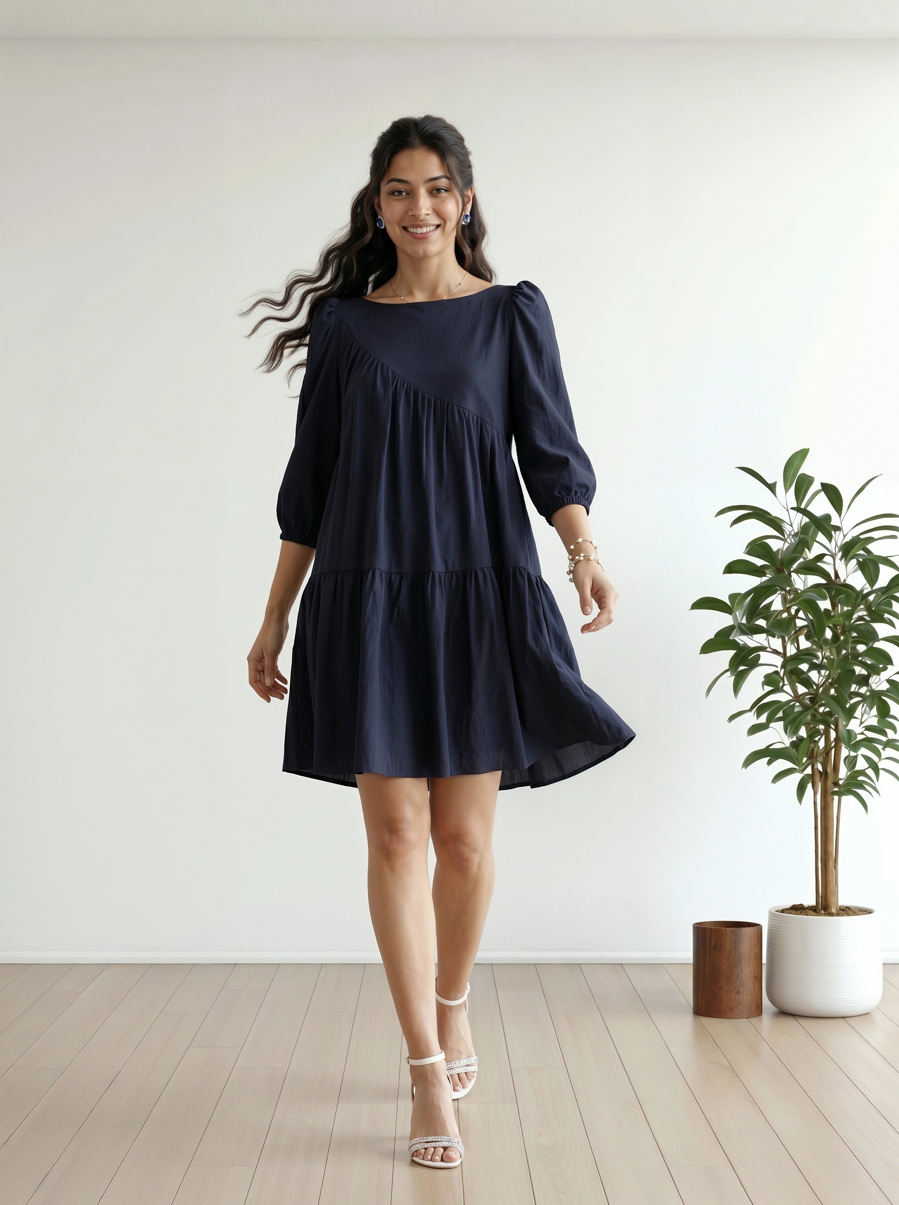 Woman wearing a navy blue dress standing in a room with a white wall and a plant.