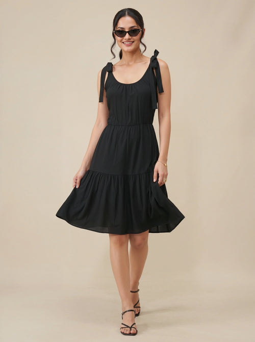 Woman wearing a black dress with bow straps on a beige background