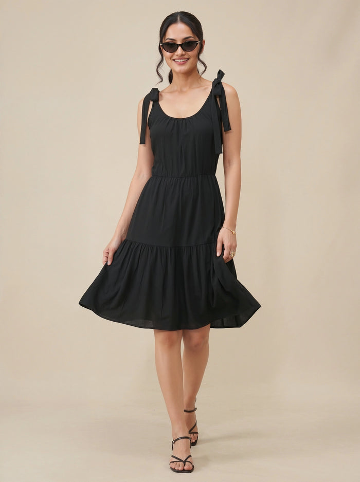 Woman wearing a black dress with bow straps on a beige background