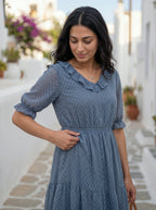Woman in a blue dress standing on a stone path with white buildings and plants in the background
