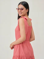 Woman wearing a pink dress with cut-out shoulders against a plain background