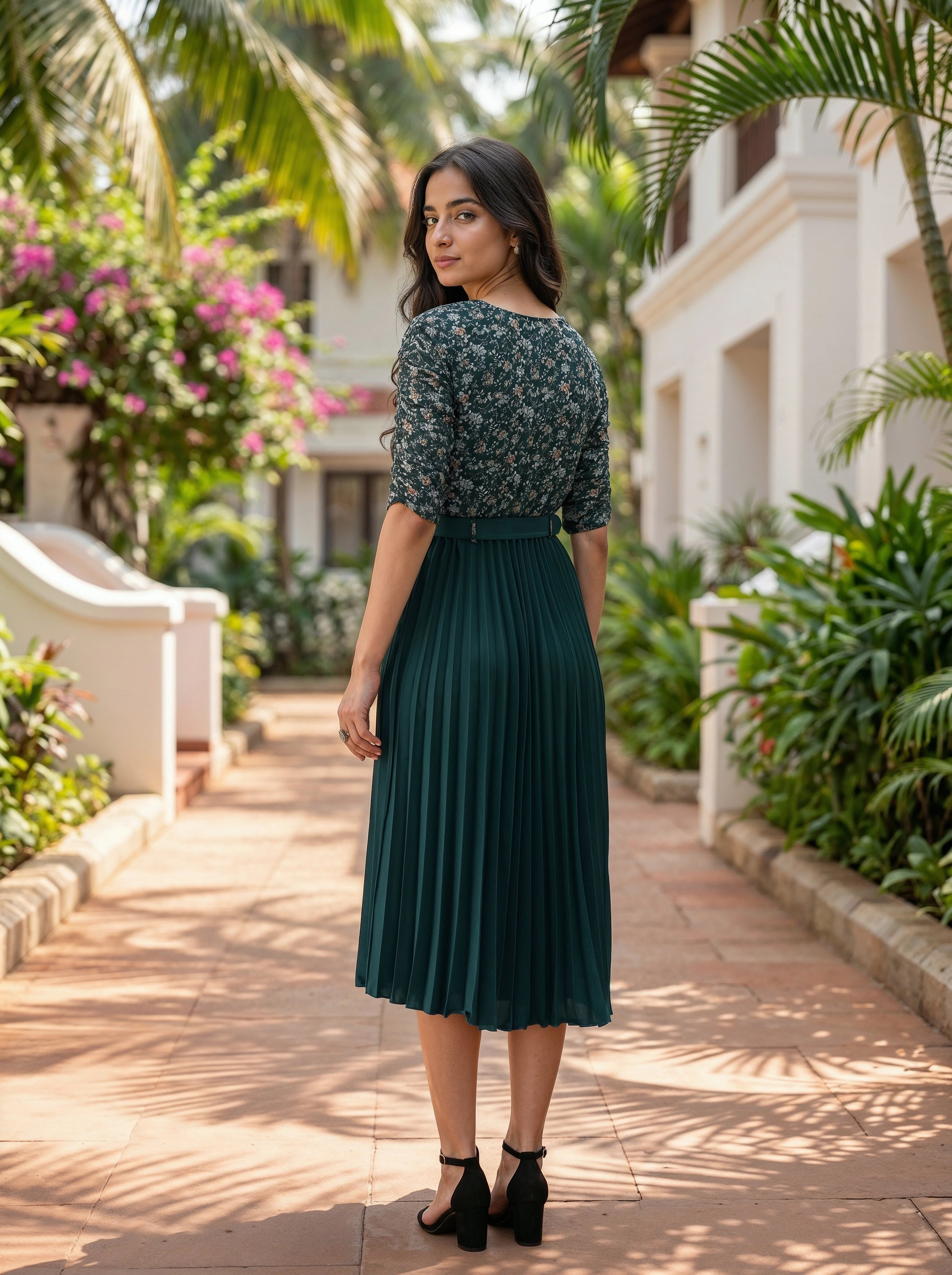 Woman in a floral top and green pleated skirt standing in a garden setting.