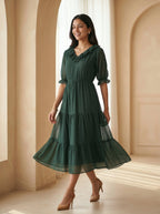 Woman wearing a green dress standing in a softly lit room with beige walls and floor.