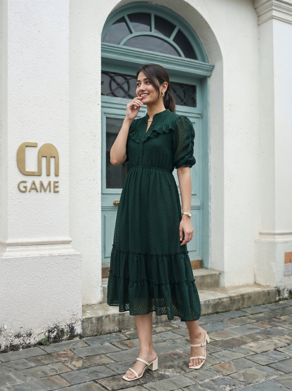 Woman in a green dress standing in front of a building with 'CM Game' logo.