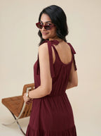 Woman in a burgundy dress with bow straps standing against a beige background