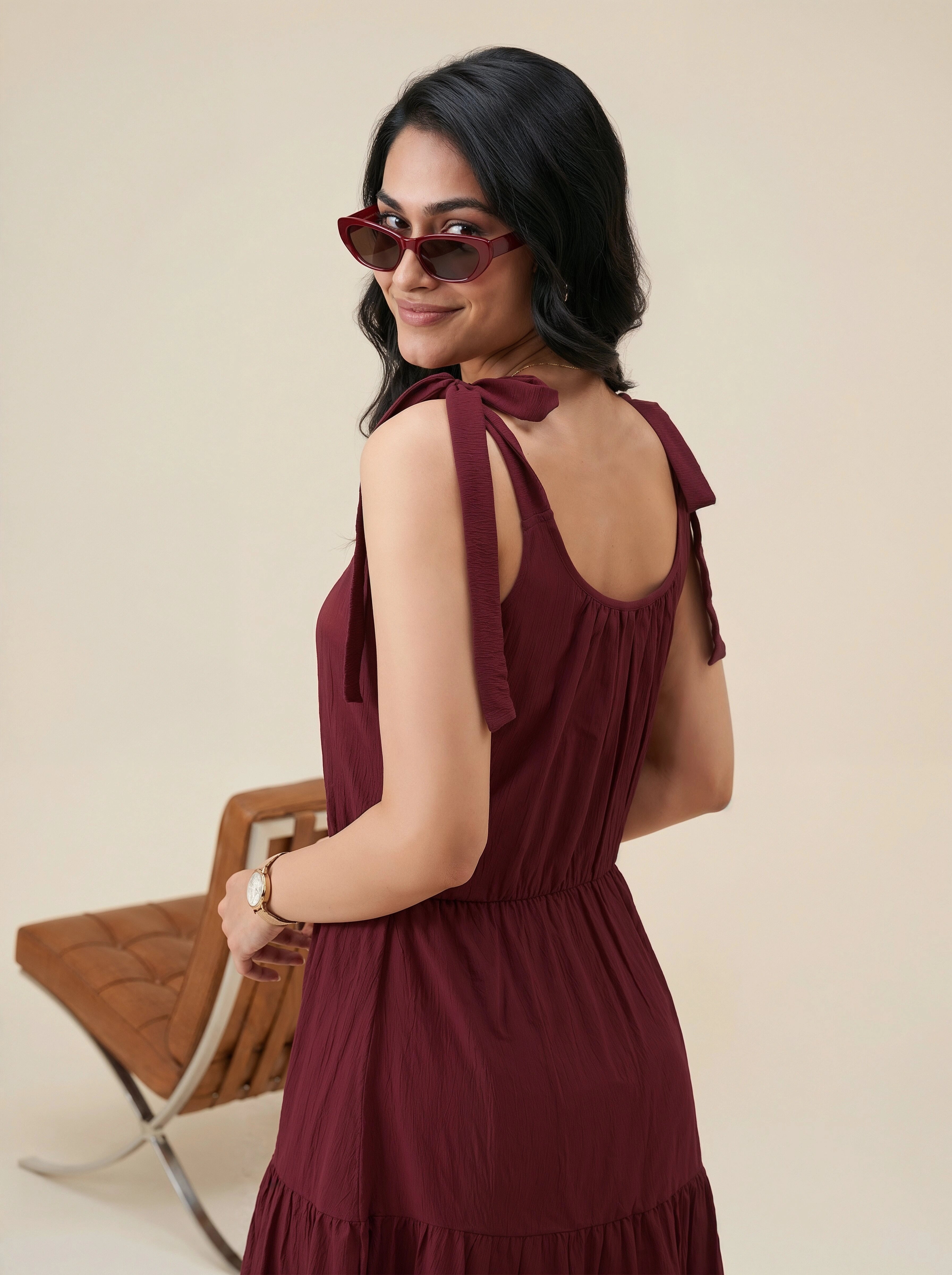 Woman in a burgundy dress with bow straps standing against a beige background