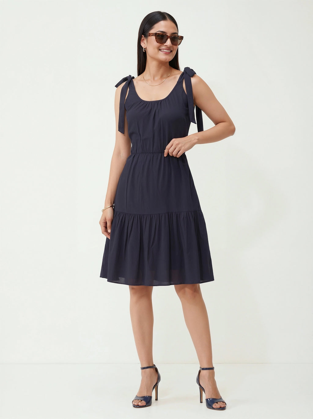 Woman wearing a navy blue dress with bow straps on a white background
