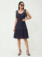 Woman wearing a navy blue dress with bow straps on a white background
