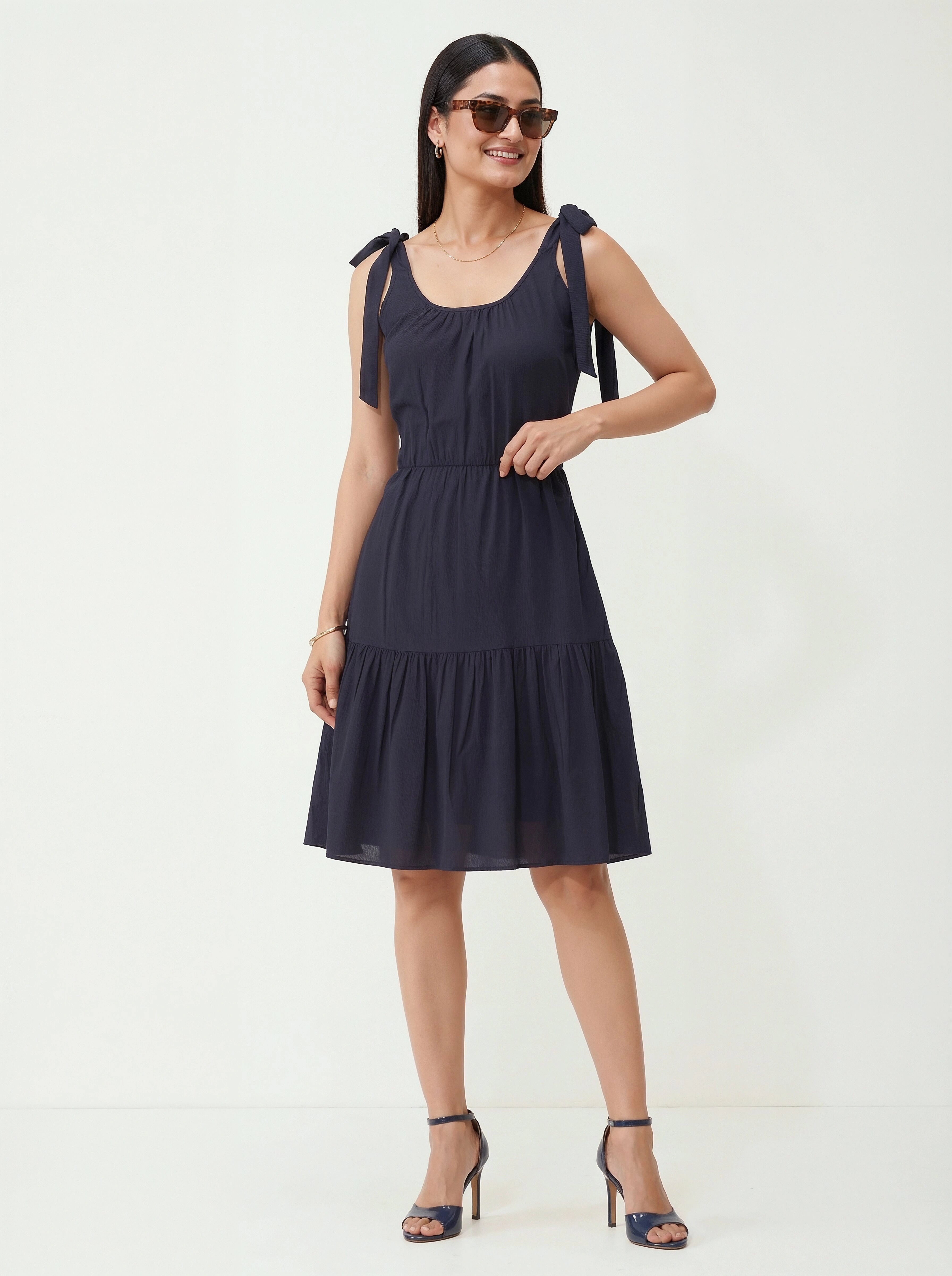 Woman wearing a navy blue dress with bow straps on a white background