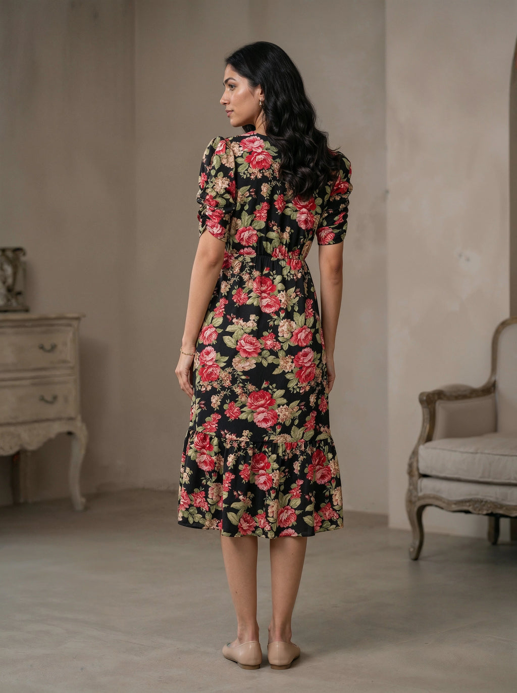 Woman wearing a floral dress in a room with a beige wall and a chair.