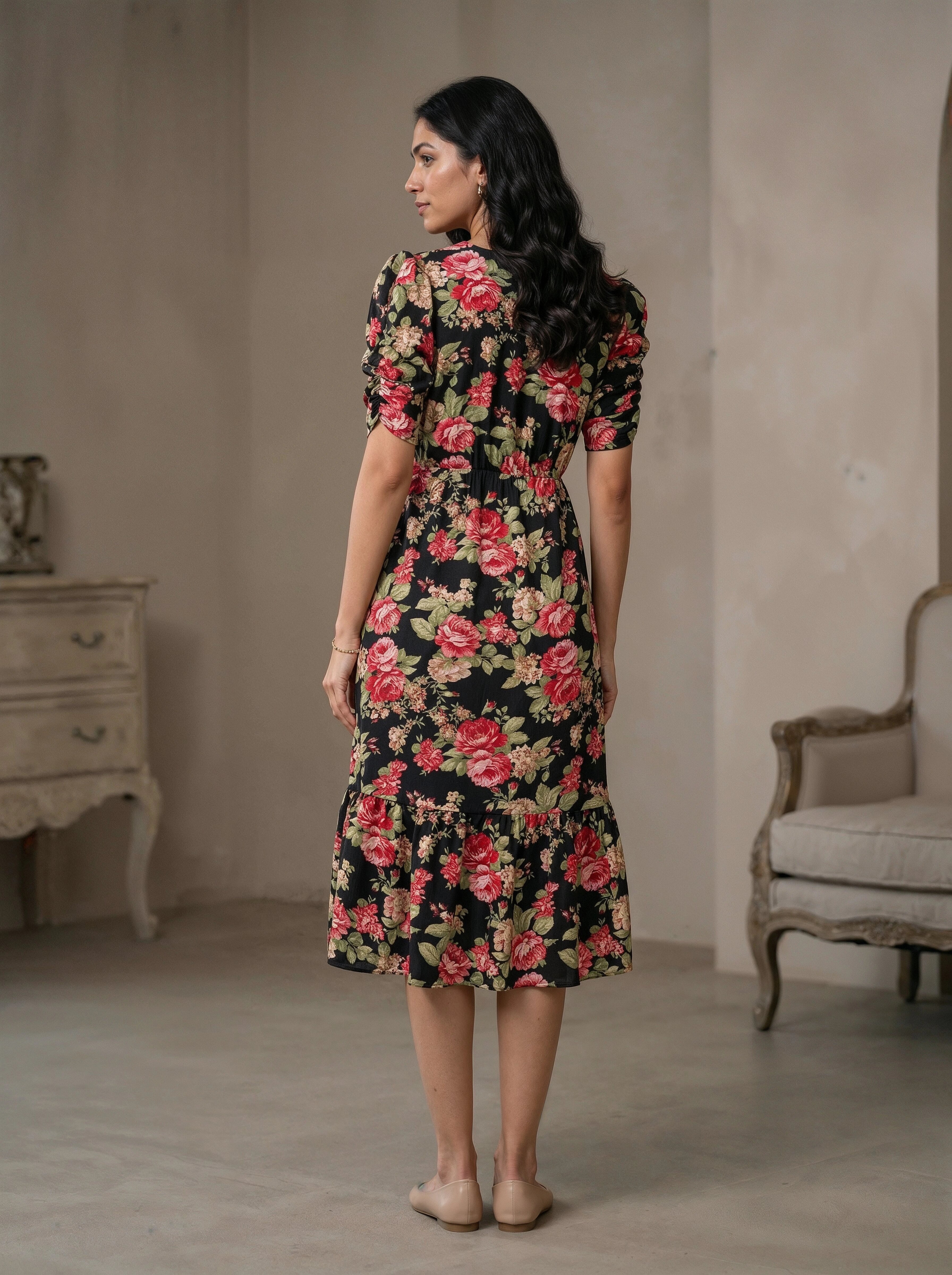 Woman wearing a floral dress in a room with a beige wall and a chair.