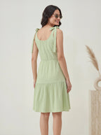 Woman wearing a light green dress with bow straps against a plain background