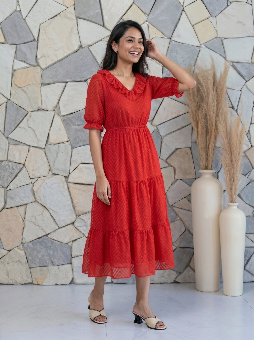 Woman in a red dress standing against a stone wall with decorative vases.