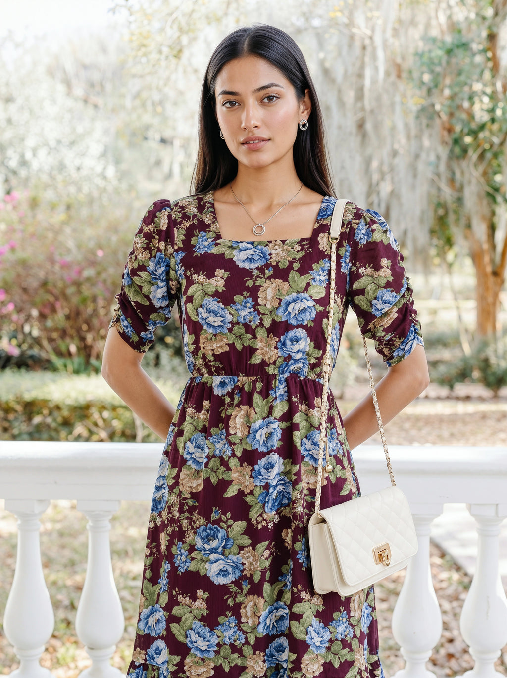 A woman modeling a dark teal blue tiered midi dress with sheer three-quarter sleeves, shown from a three-quarter back angle against a light gray studio background.