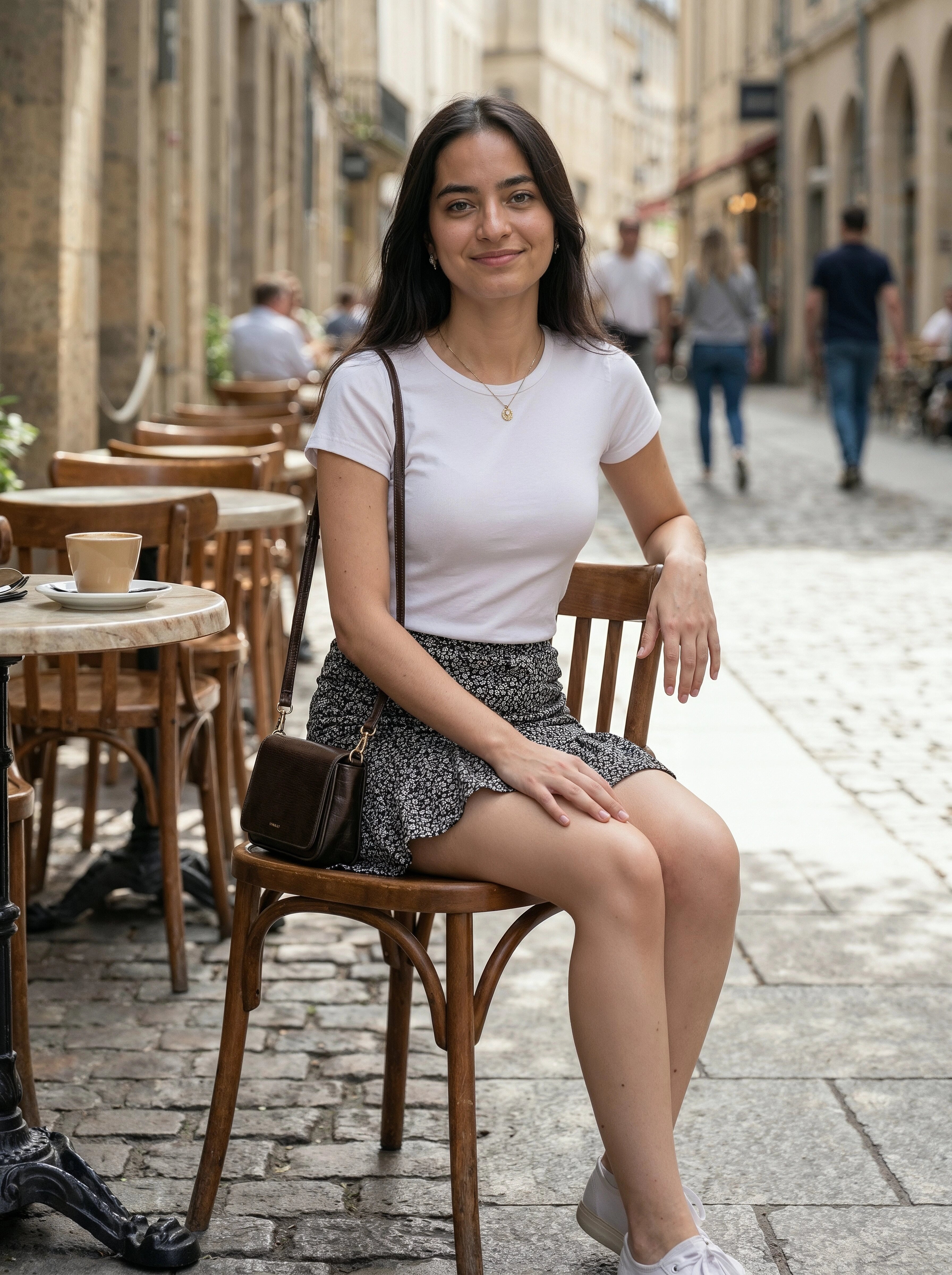 Woman sitting on a wooden chair in an outdoor cafe setting with people and buildings in the background.