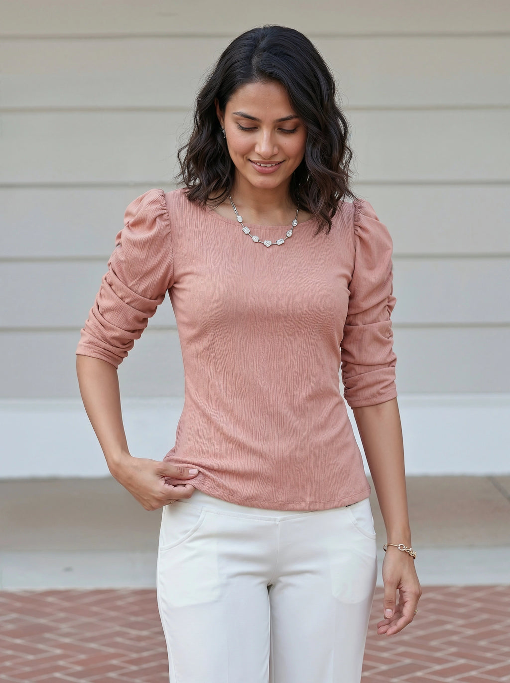 Woman wearing a pink top with ruffled sleeves and white pants outdoors.