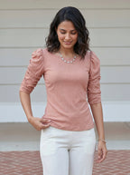 Woman wearing a pink top with ruffled sleeves and white pants outdoors.