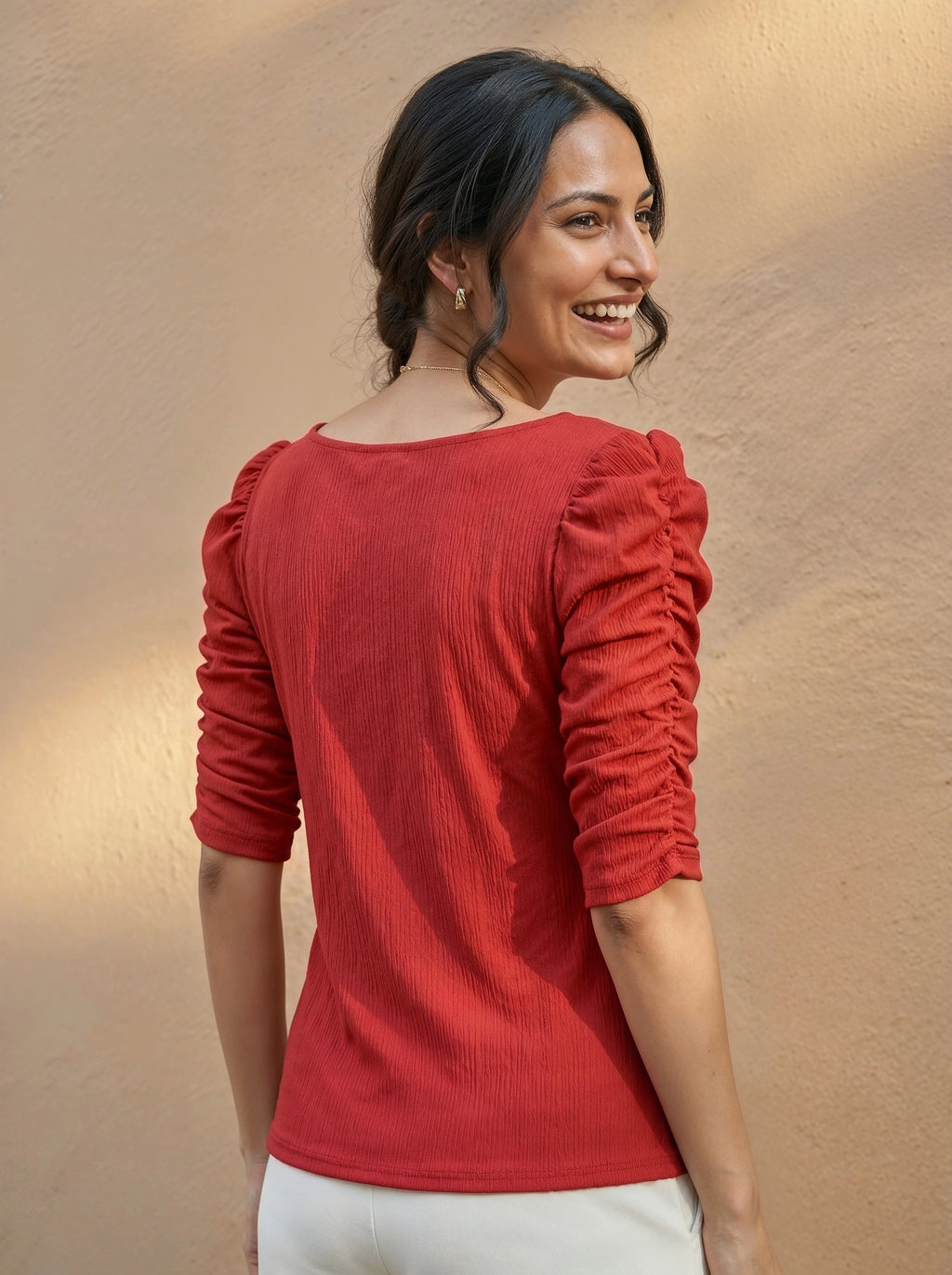 Woman wearing a red blouse with puffed sleeves against a beige background