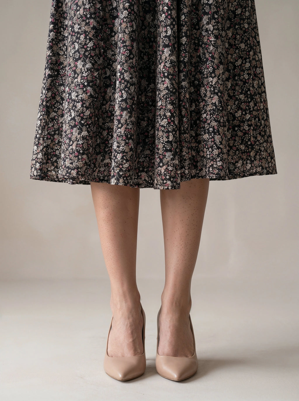Person wearing a floral dress and beige heels on a neutral background