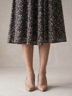 Person wearing a floral dress and beige heels on a neutral background
