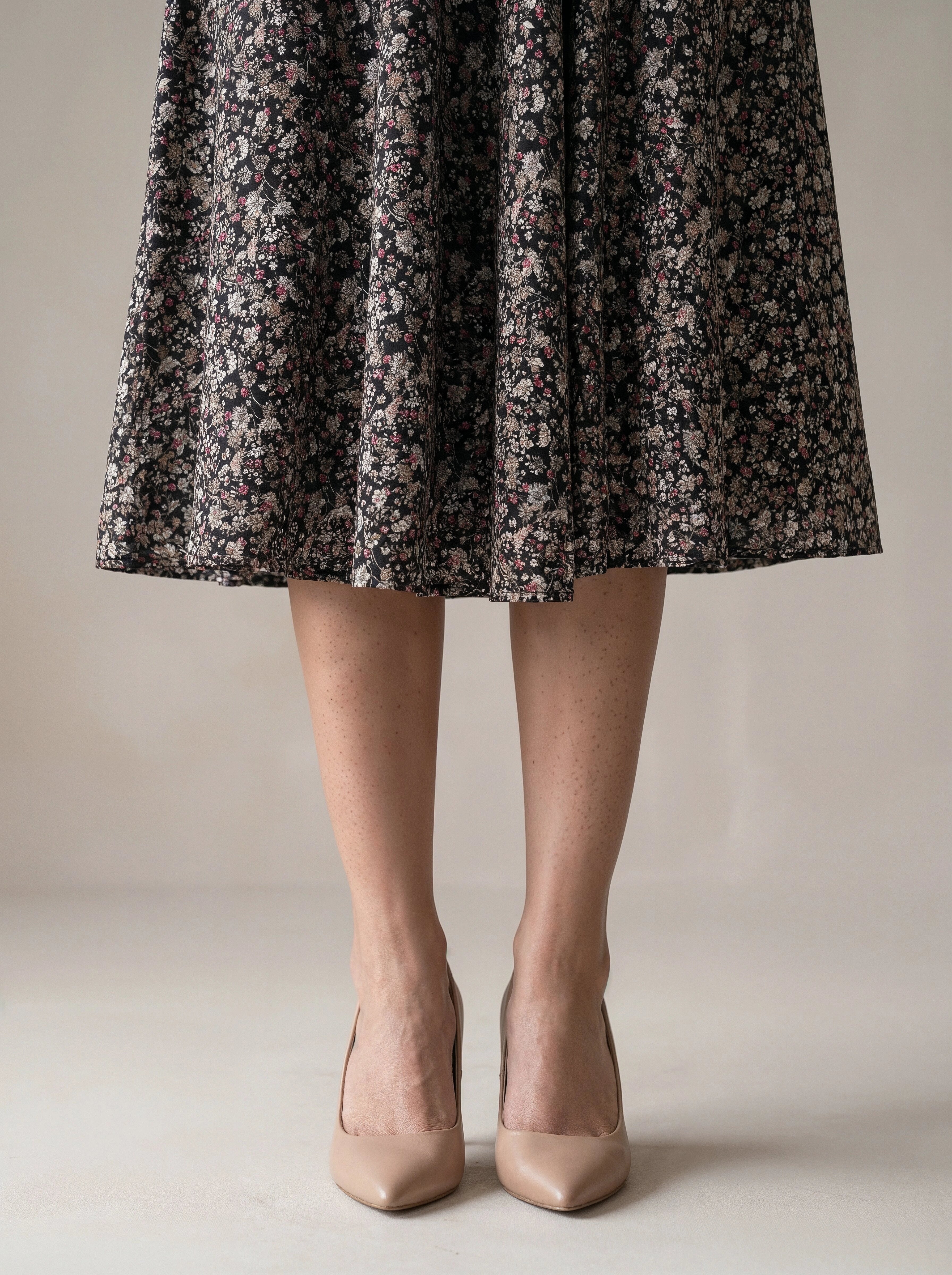 Person wearing a floral dress and beige heels on a neutral background