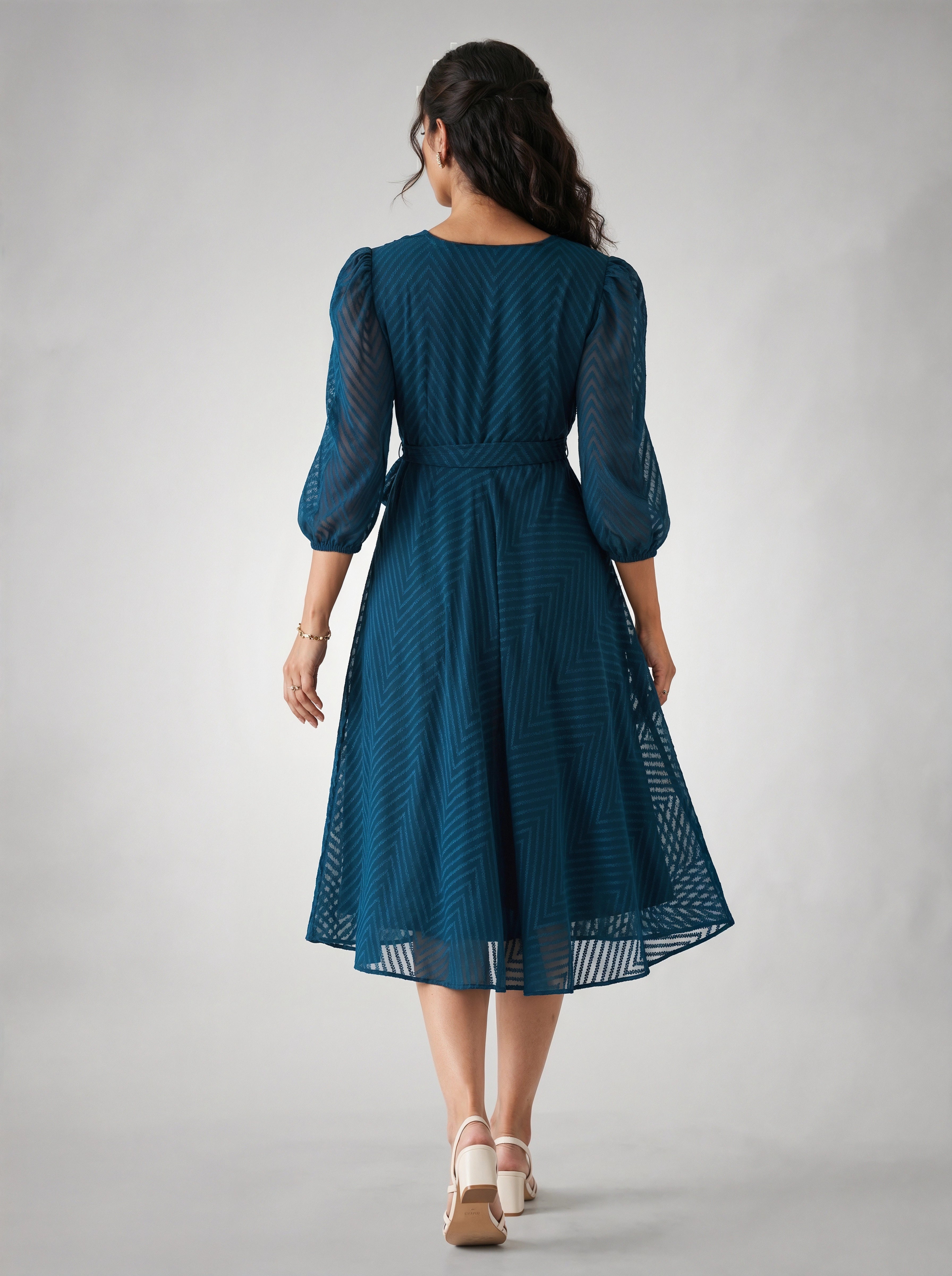 Woman wearing a blue dress with a subtle pattern on a plain background