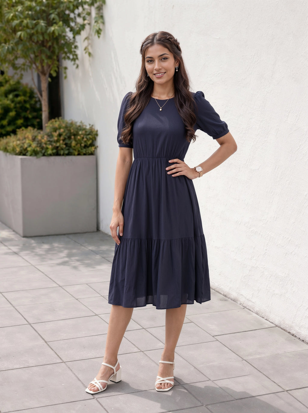 Woman in a navy blue dress standing outdoors on a tiled pavement.
